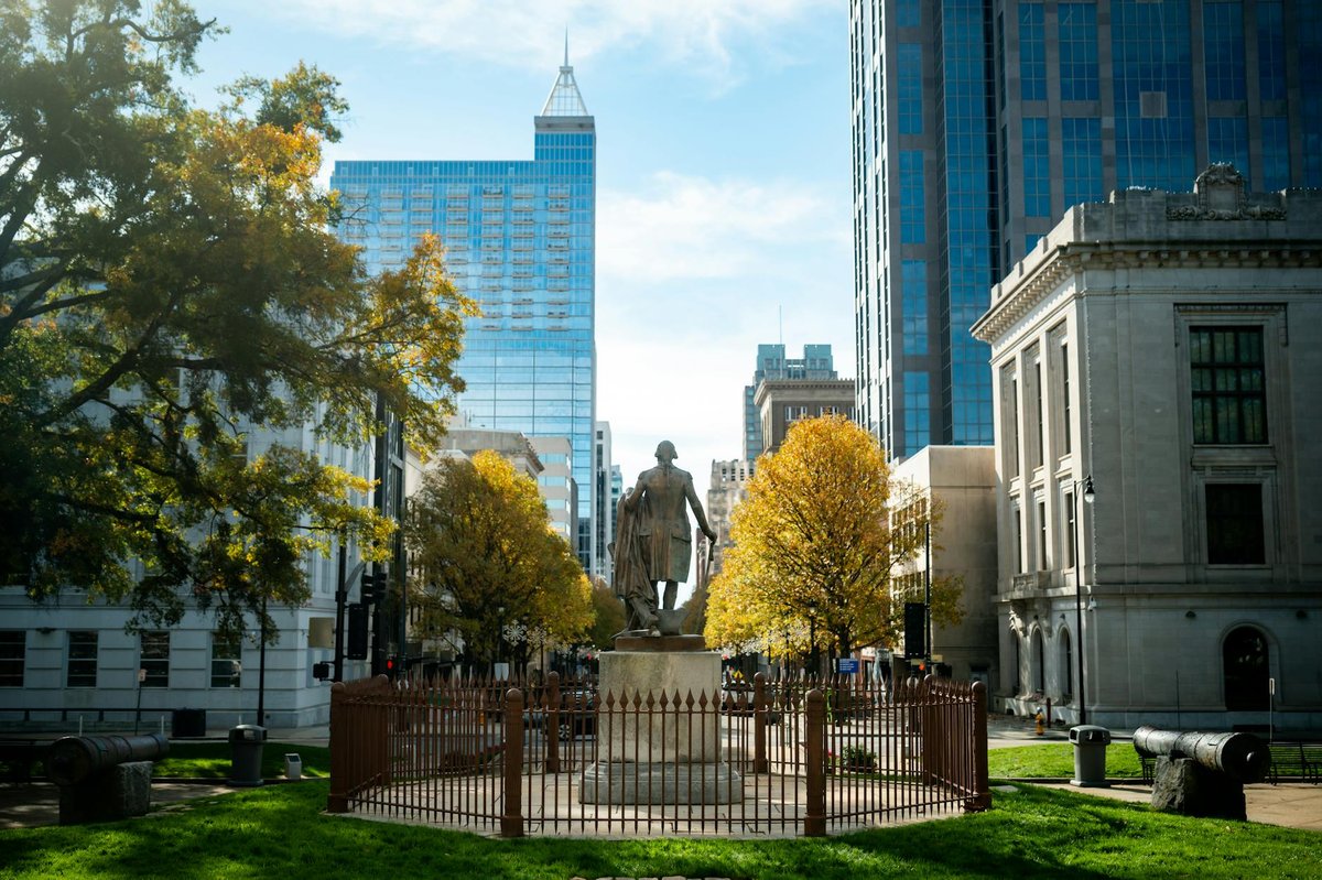 Statue in downtown Raleigh with skyscrapers and fall foliage.