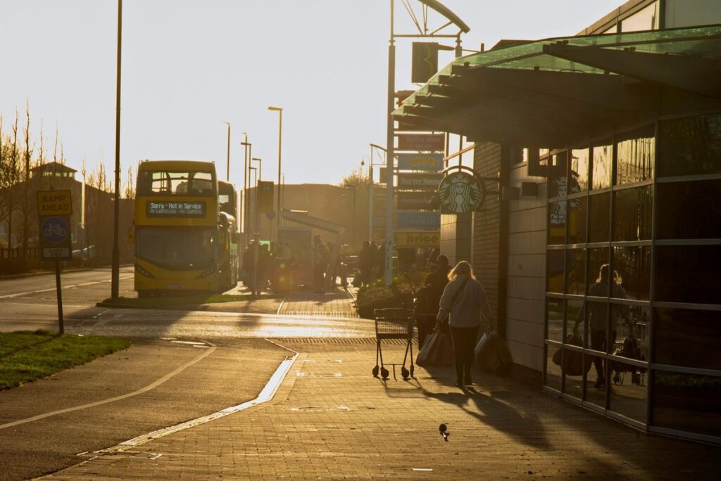 Shoppers navigate the sidewalk as a 'Not in Service' bus passes by in Dublin at sunset.
