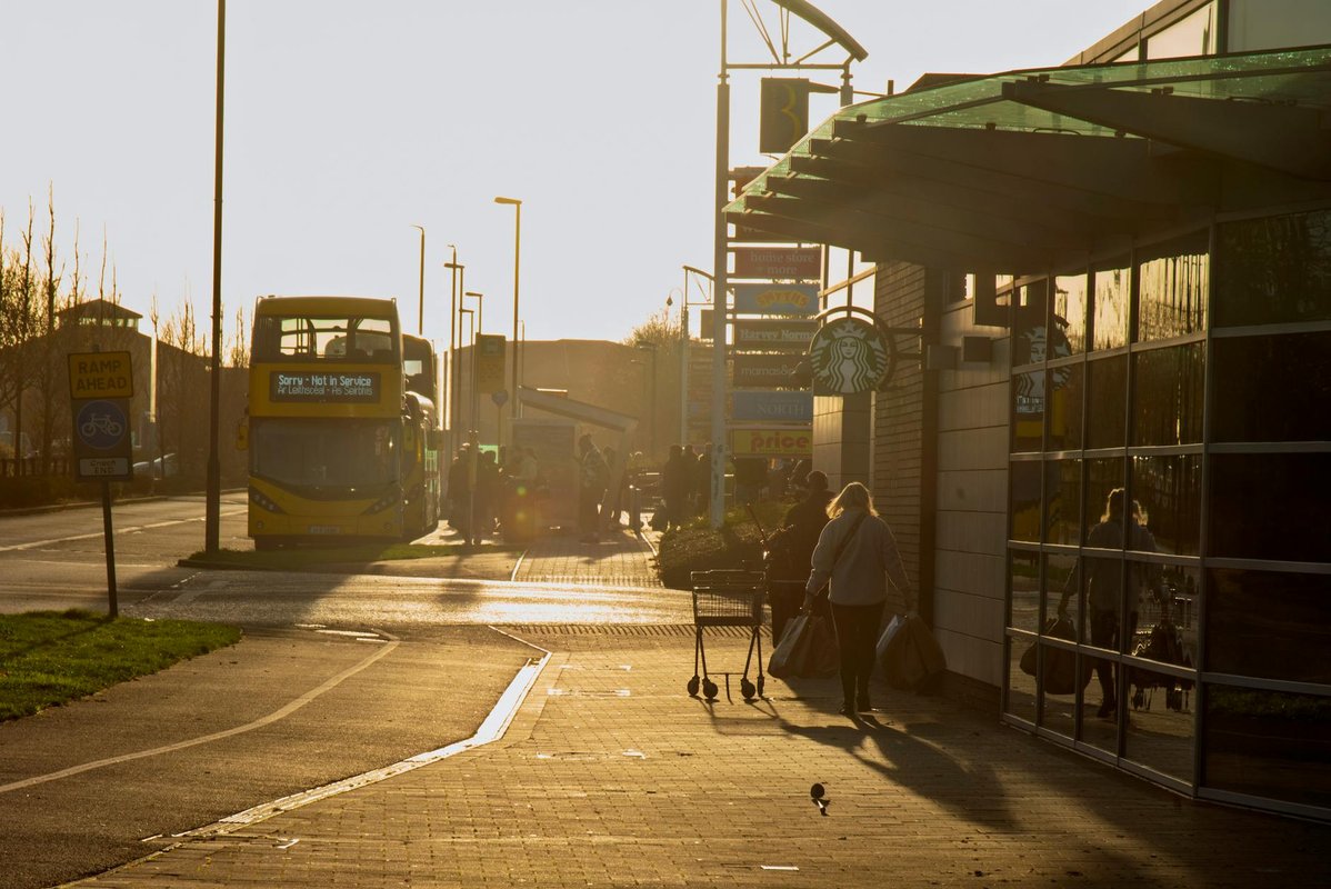 Shoppers navigate the sidewalk as a 'Not in Service' bus passes by in Dublin at sunset.