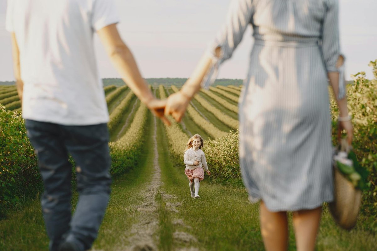 A family holds hands with their child in a beautiful, green field under a clear sky.