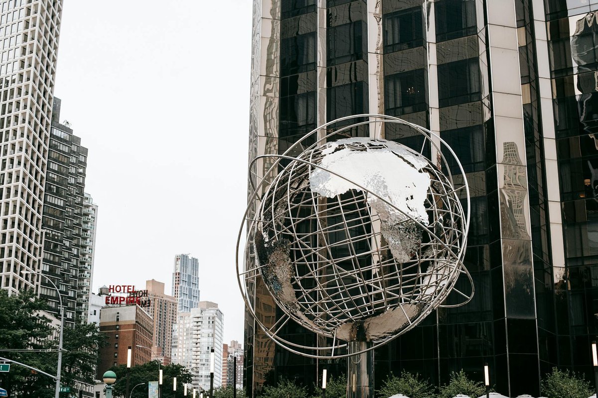 Contemporary stainless steel unisphere sculpture located near modern skyscrapers against Trump tower on street in New York city on Manhattan