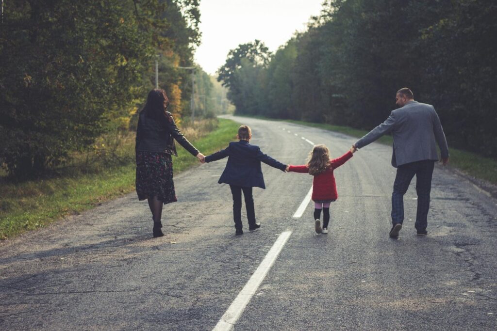 Joyful family holding hands walking on a quiet country road, enjoying nature and togetherness.