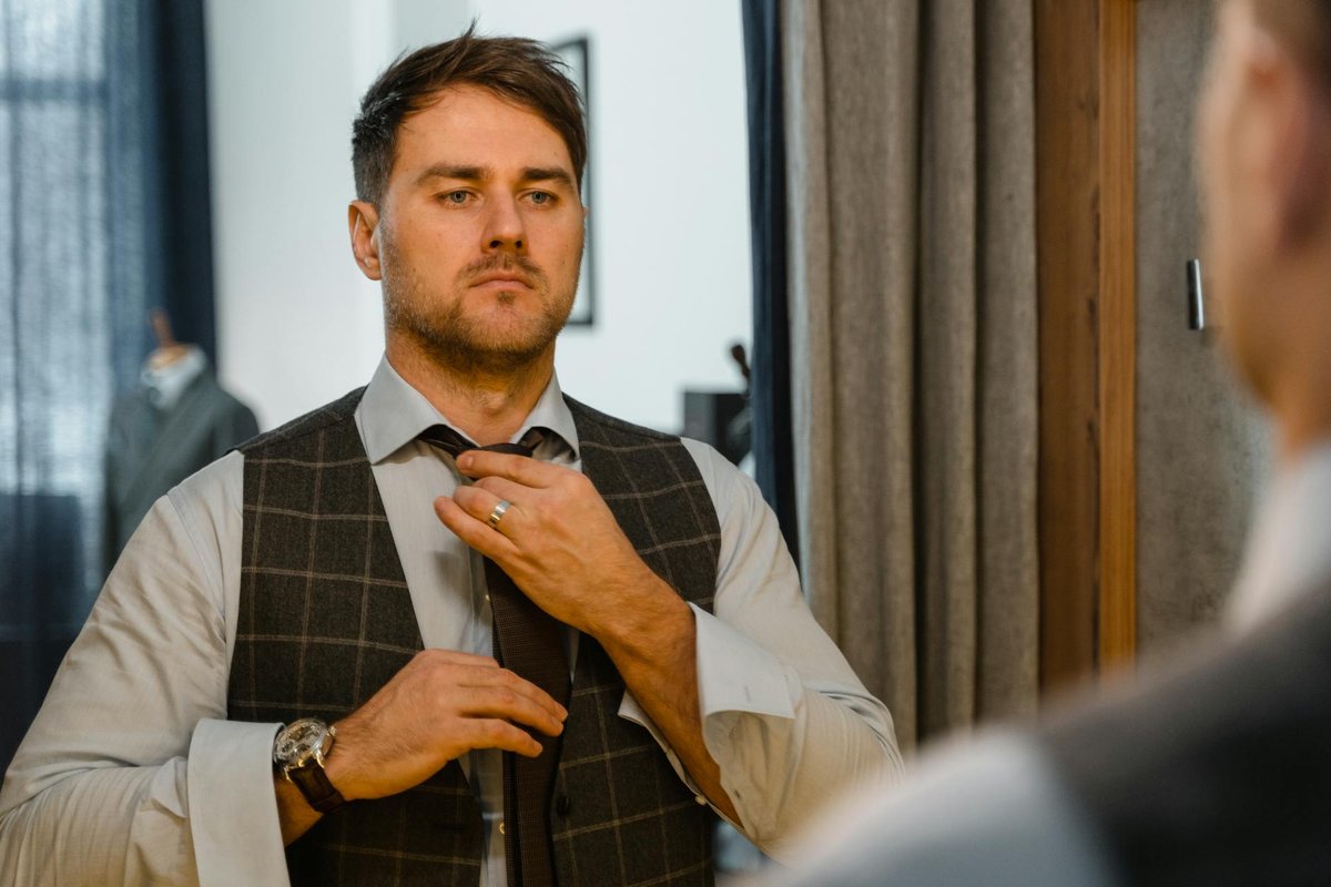 Confident man perfecting his necktie in a mirror reflection, showcasing style and elegance.