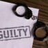 Top view of handcuffs on paper with 'GUILTY' text, symbolizing a verdict or crime.