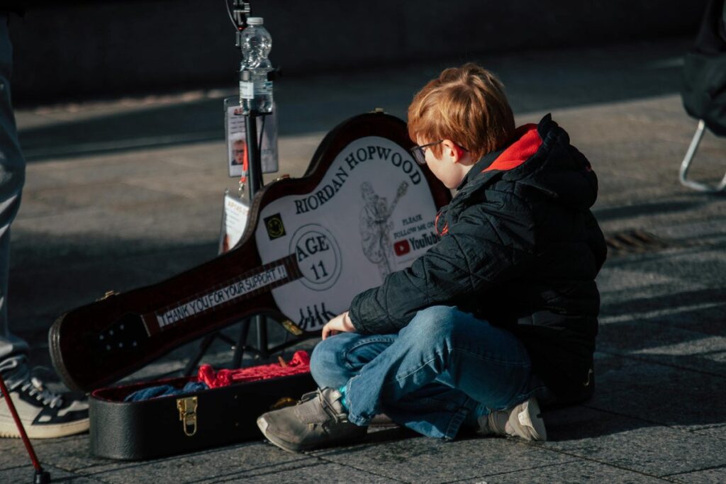 A child sits with a guitar case in Dublin, capturing the essence of street performance.