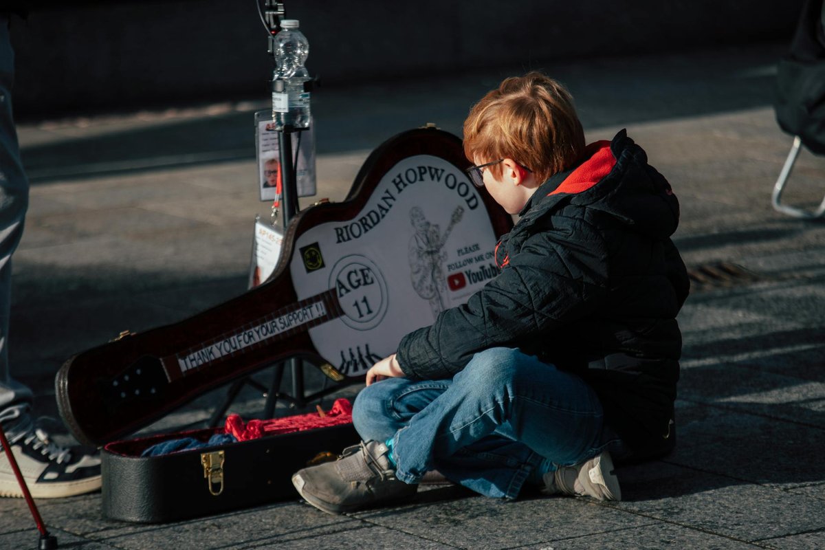 A child sits with a guitar case in Dublin, capturing the essence of street performance.