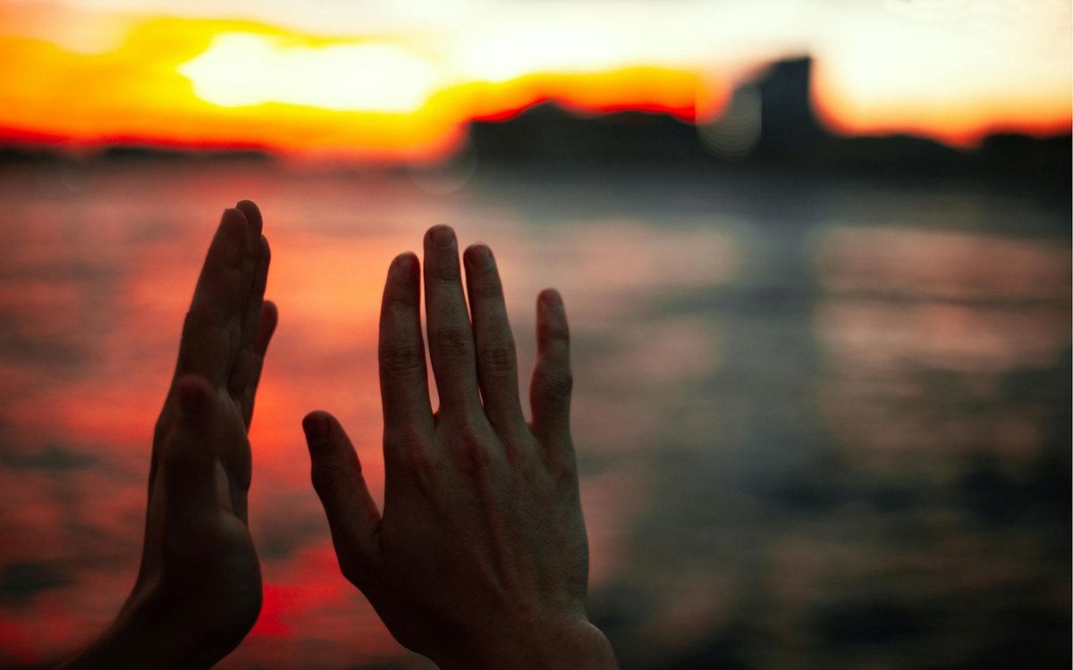 A serene moment as hands frame a vivid orange sunset over calm ocean waters.