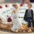Close-up of a wedding cake with bride and groom figurines, raspberries, and whipped cream.