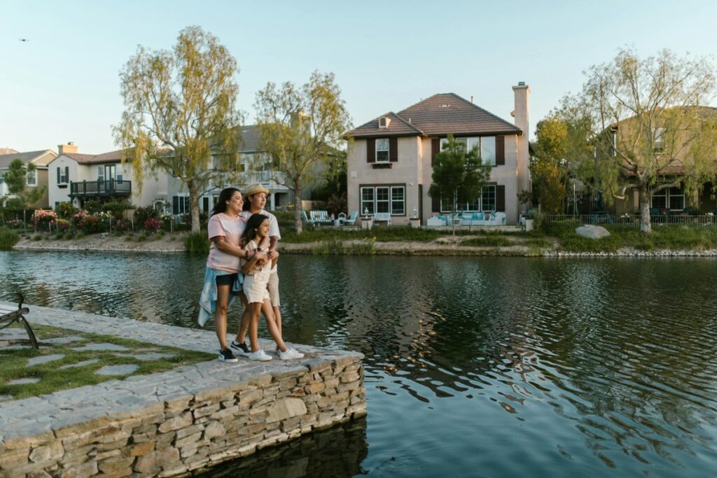 A family embraces by a lakeside in a picturesque urban neighborhood, capturing a moment of love and togetherness.