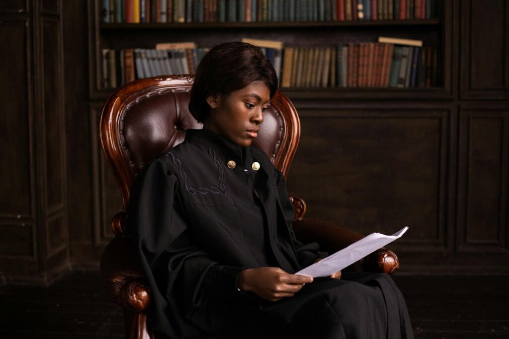 A woman reading papers in an elegant library, sitting on a vintage chair.