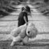 Monochrome image of a child holding a teddy bear while walking down a dirt road, conveying a sense of solitude.