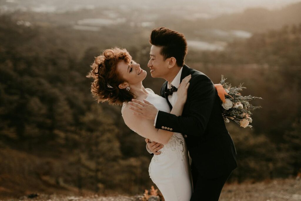 Bride and groom share a joyful embrace outdoors during a warm sunset, capturing a romantic wedding moment.