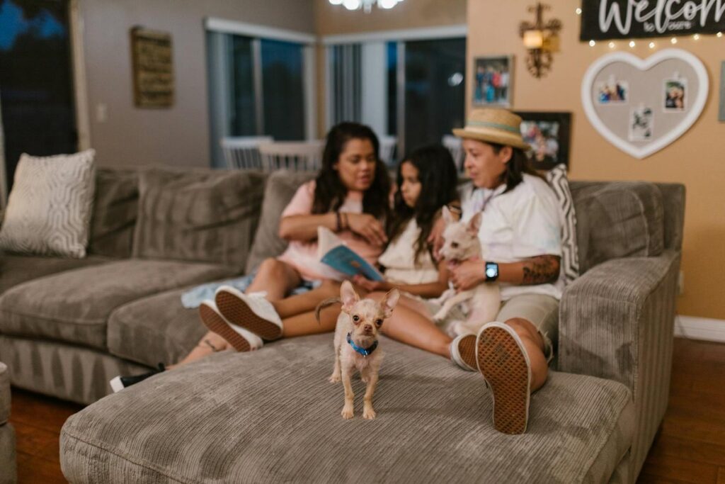 Same-sex couple with daughter and dogs enjoying family time on the couch indoors.