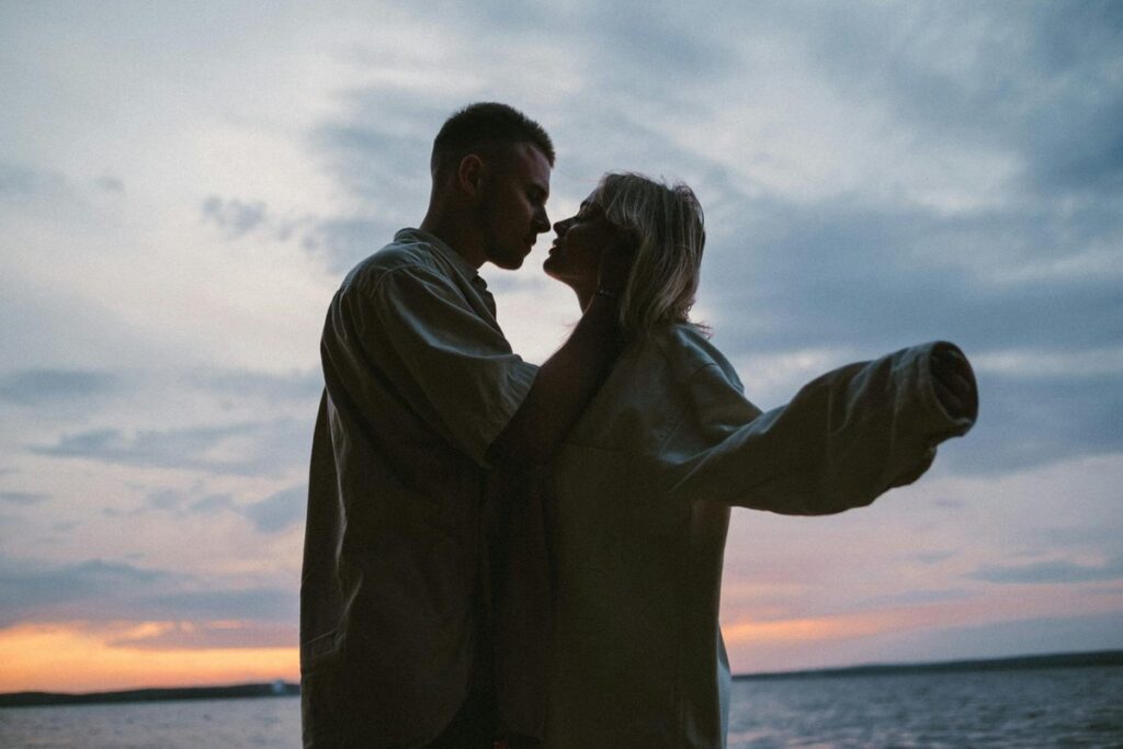 Silhouette of a loving couple embracing by the lake at sunset, capturing a romantic moment.