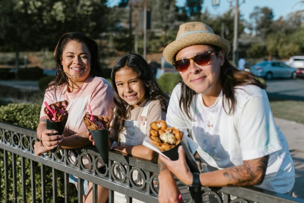A joyful family of three enjoying snacks by a wrought iron fence in a sunny outdoor setting.