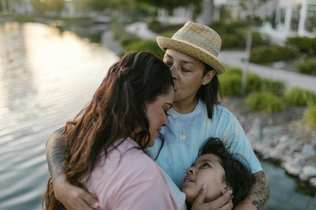 A warm and tender embrace among two women and a child by the lakeside at sunset, showcasing love and togetherness.
