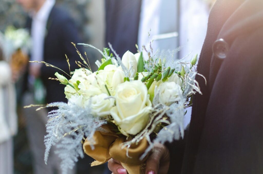 Close-up of a white rose bouquet held by a groom at an outdoor wedding ceremony.