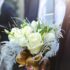 Close-up of a white rose bouquet held by a groom at an outdoor wedding ceremony.