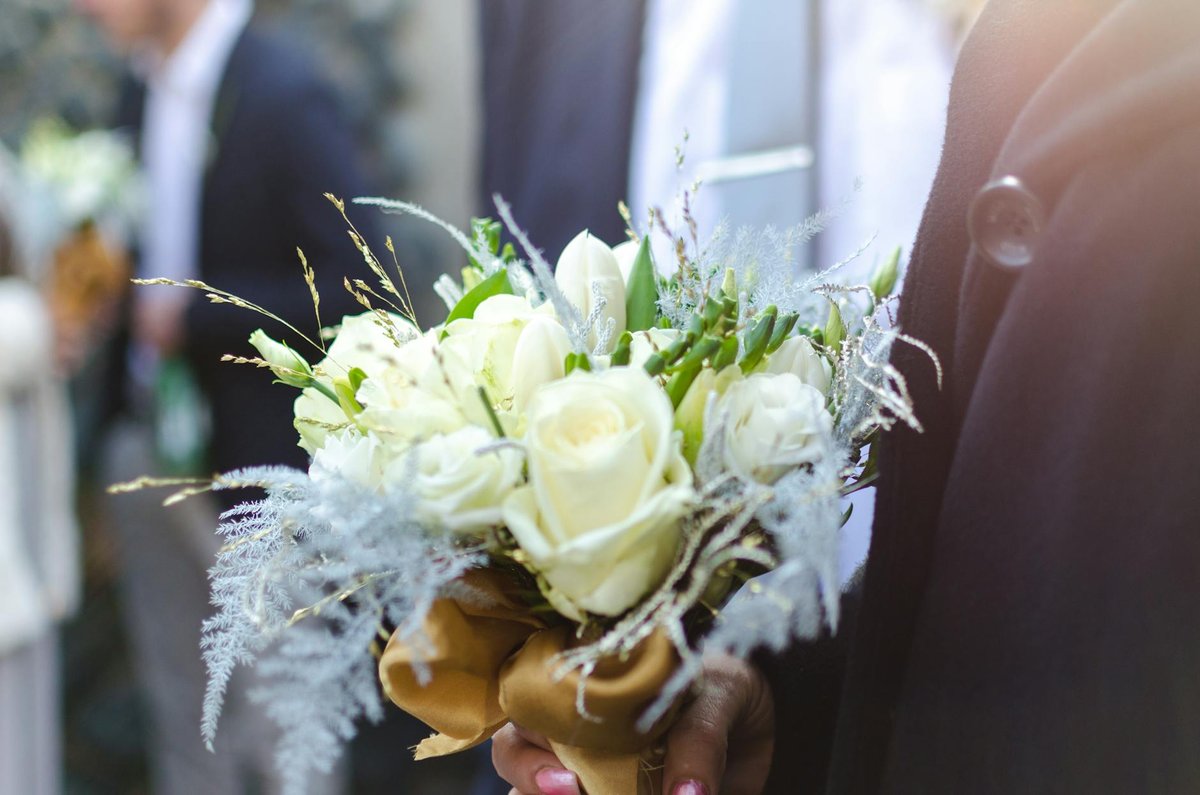 Close-up of a white rose bouquet held by a groom at an outdoor wedding ceremony.