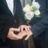 Close-up of two grooms holding hands with wedding rings and bouquet, symbolizing love and commitment.