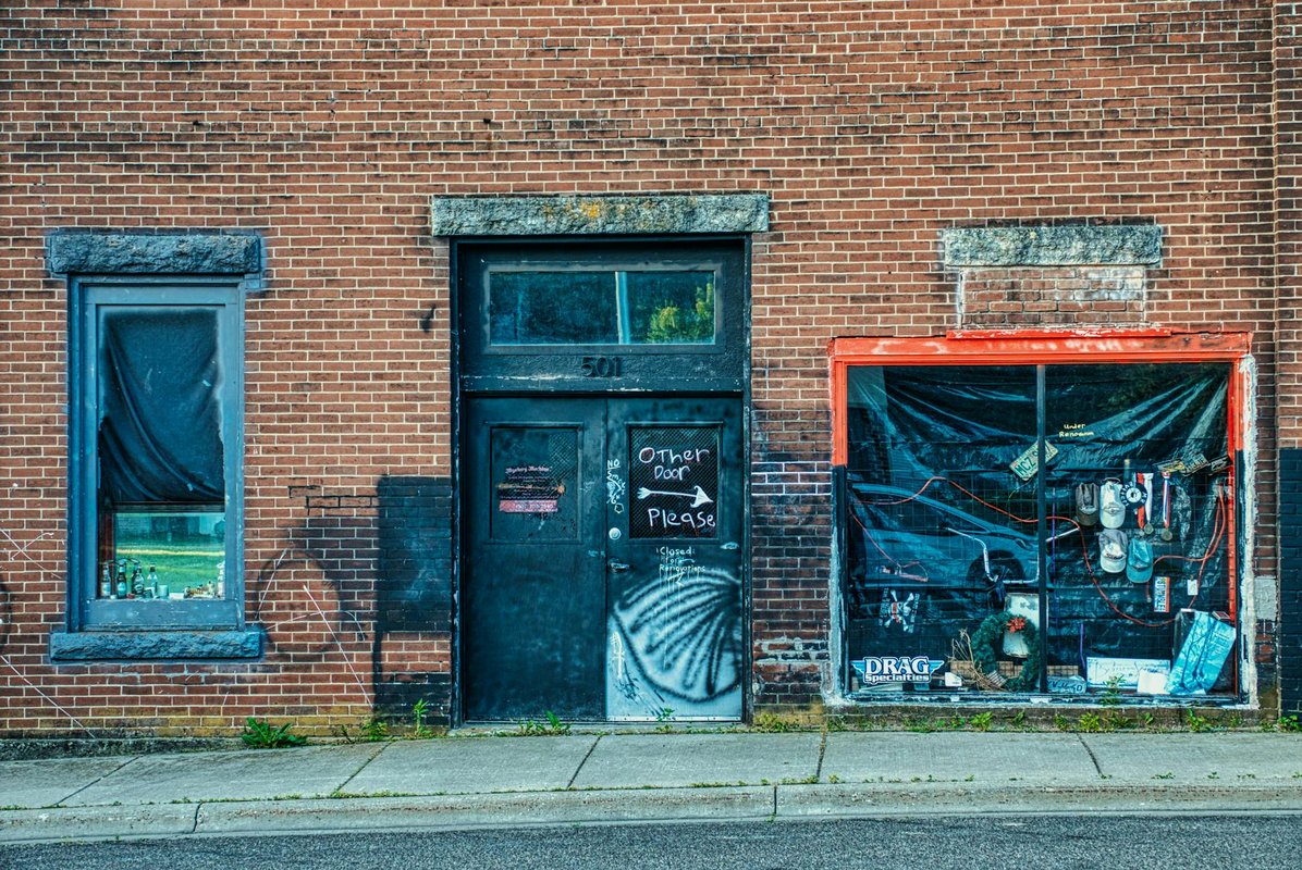A grungy abandoned storefront with a brick facade and closed door in Millville, Minnesota.