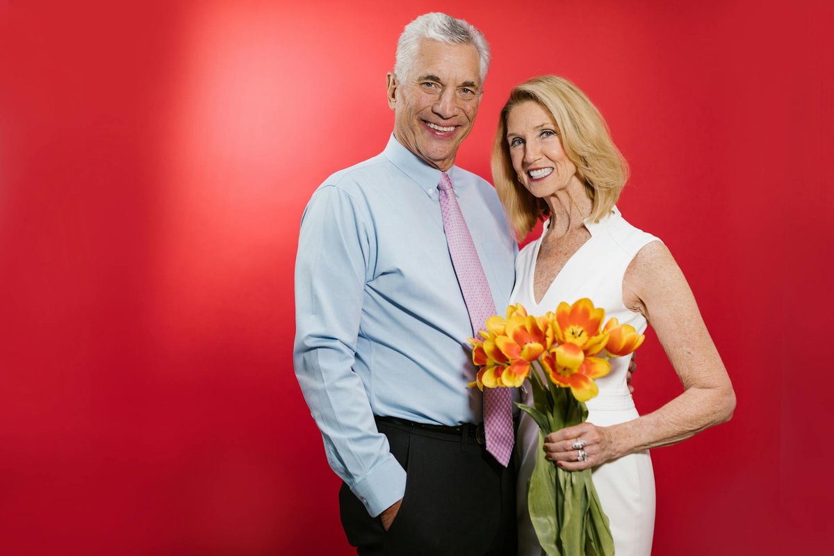 A senior couple poses with tulips against a vibrant red backdrop, exuding joy and love.