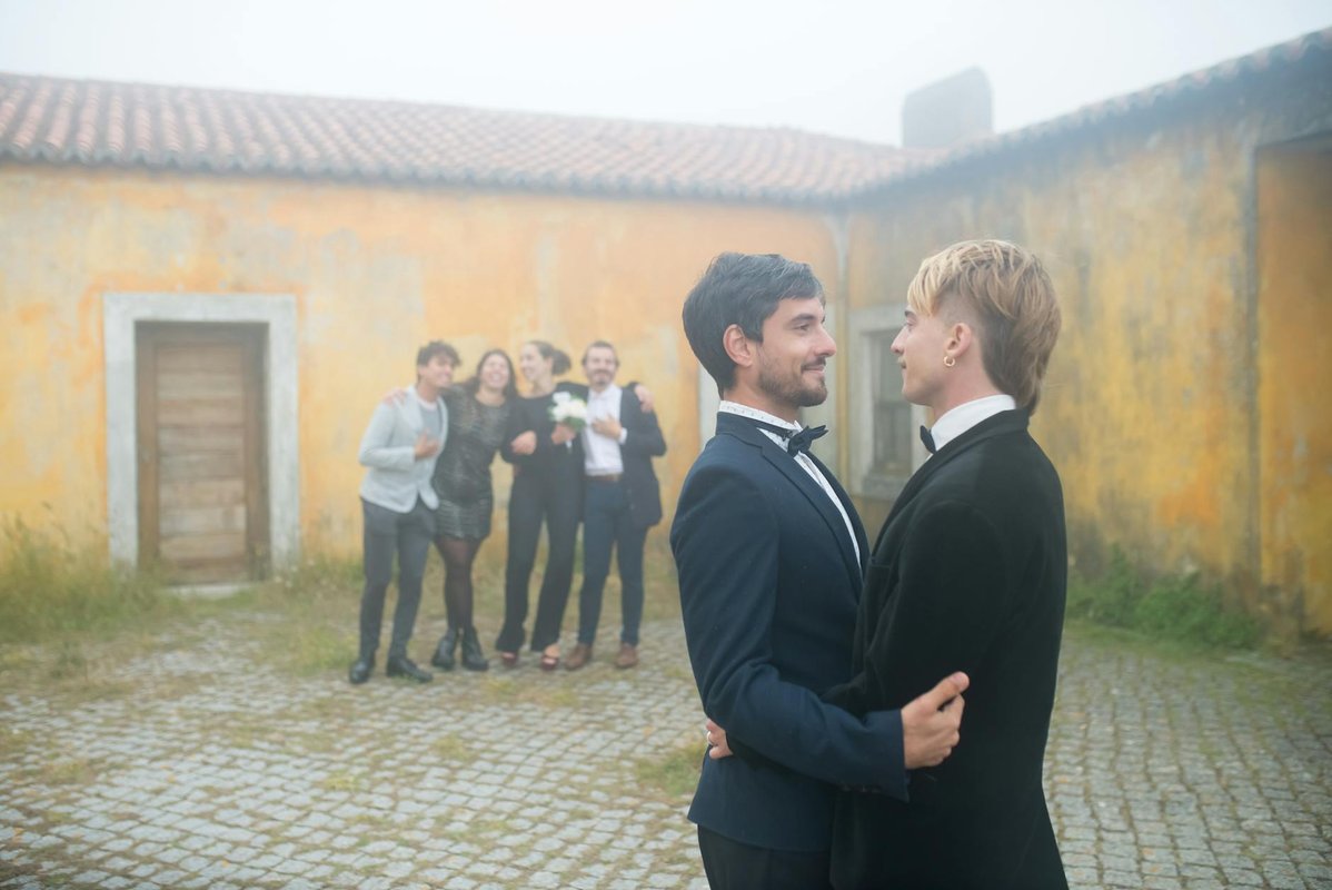 A joyful gay couple celebrating their wedding outdoors with friends in Portugal.