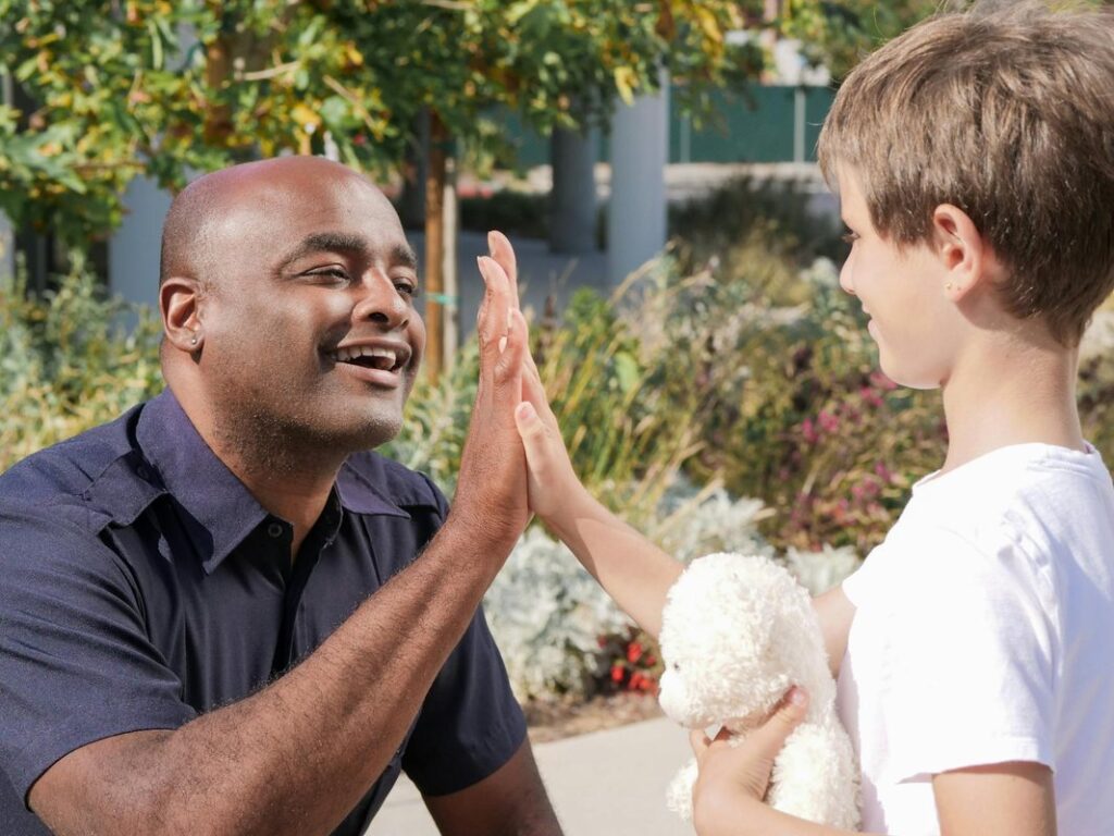 Police officer and child high-fiving outdoors, symbolizing community engagement.