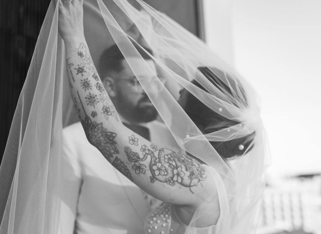 Artistic black and white photo of a bride and groom sharing an intimate moment with a veil.