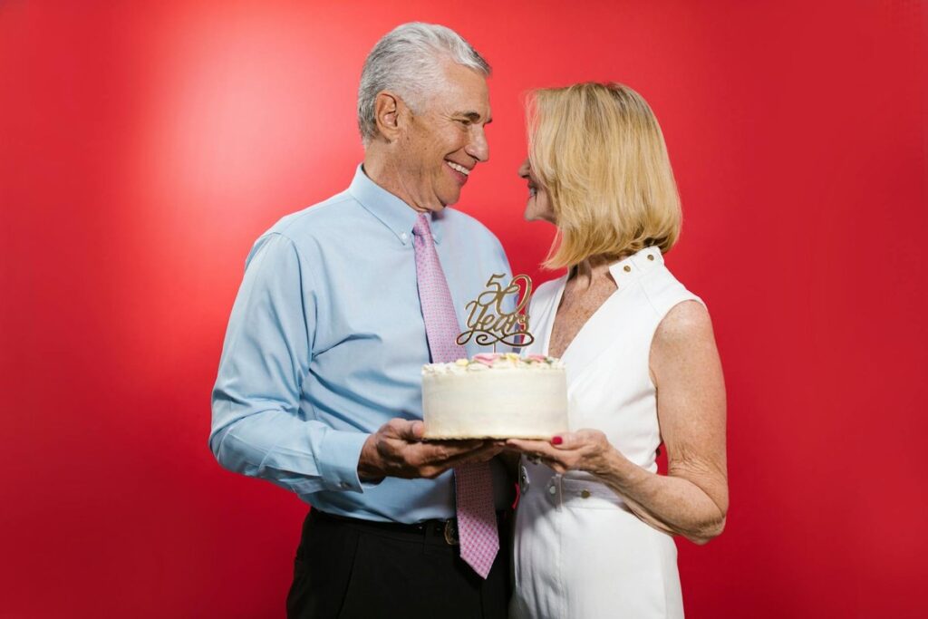 Happy senior couple celebrating their 50th anniversary with cake in a studio setting.