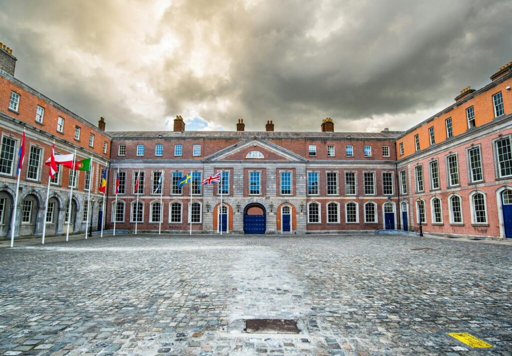 Historic Dublin Castle courtyard with flags, showcasing classic architecture under a moody sky.