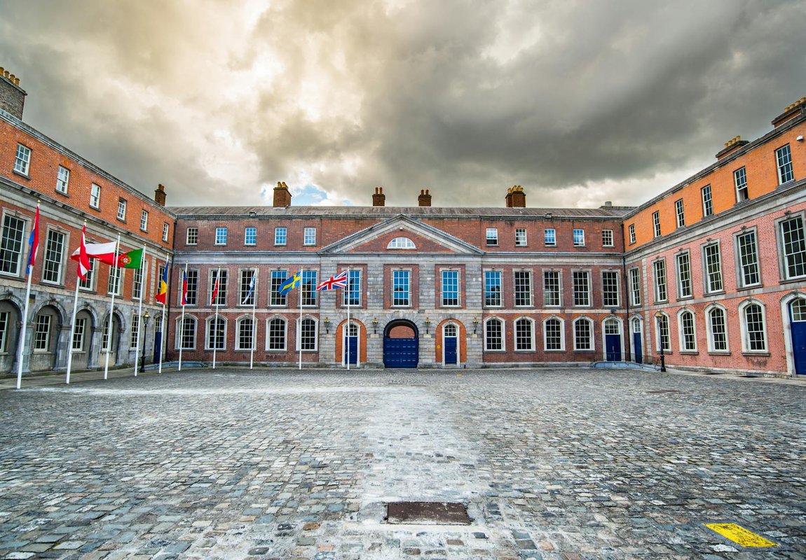 Historic Dublin Castle courtyard with flags, showcasing classic architecture under a moody sky.