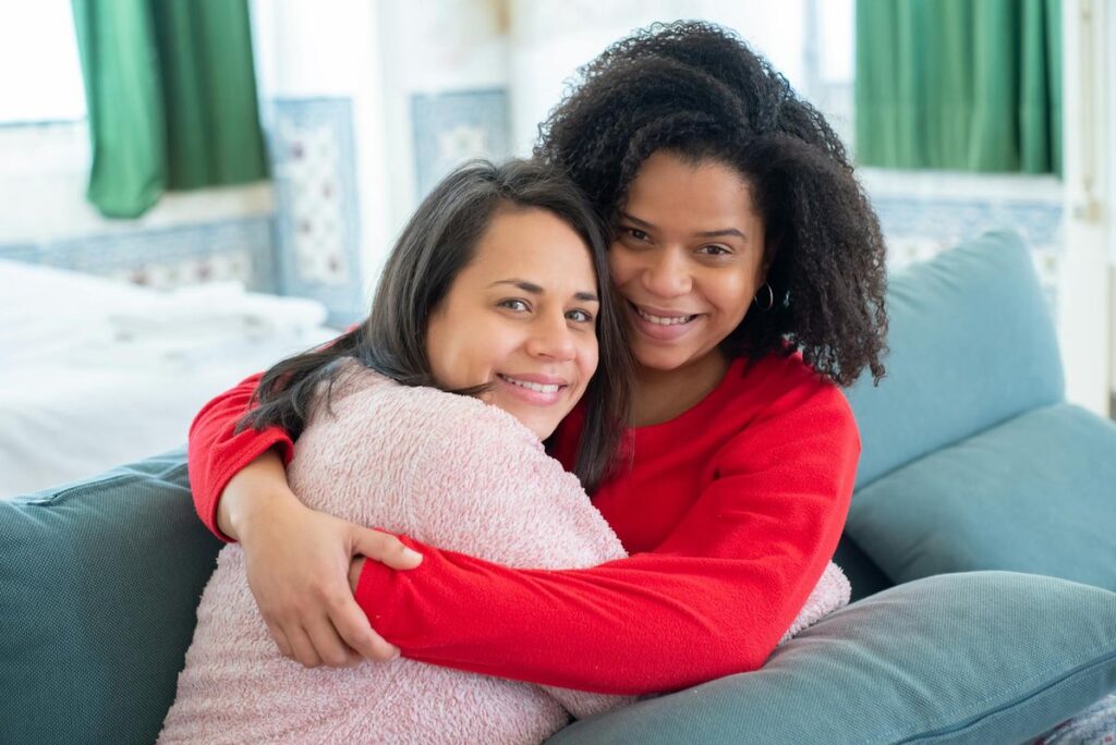 A happy lesbian couple embraces on a sofa, exuding warmth and love in a cozy indoor setting.