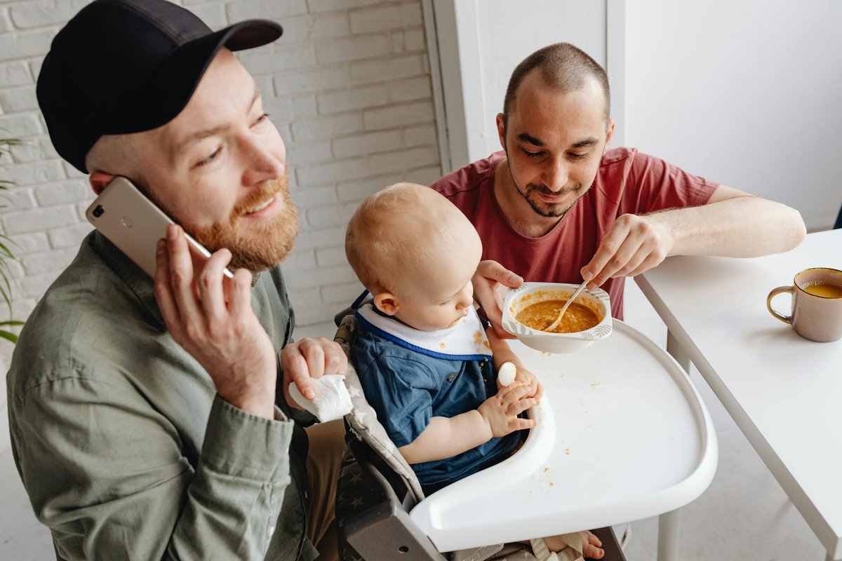 Loving same-sex couple feeding their child at breakfast, showcasing family diversity.