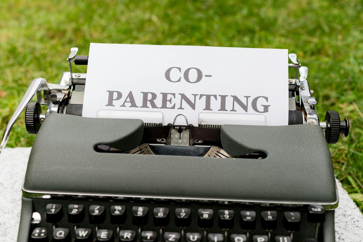 Close-up of an antique typewriter with 'Co-Parenting' paper, set outdoors on grass.